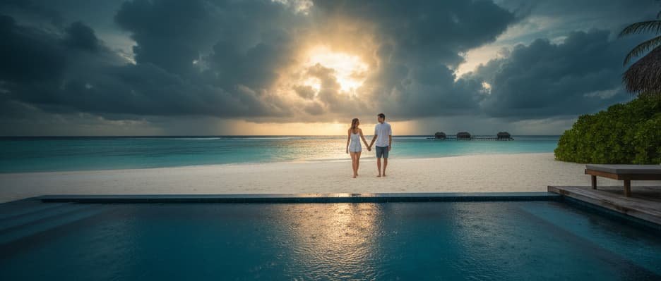 A real photograph of a couple holding hands on a white sand beach in the Maldives, viewed from a private infinity pool under a dramatic cloudy sky at sunset.