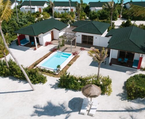 Aerial view of a Beach Residence at Joy Island Maldives with a private central pool, outdoor seating areas, thatched umbrellas, and surrounding tropical greenery on white sand