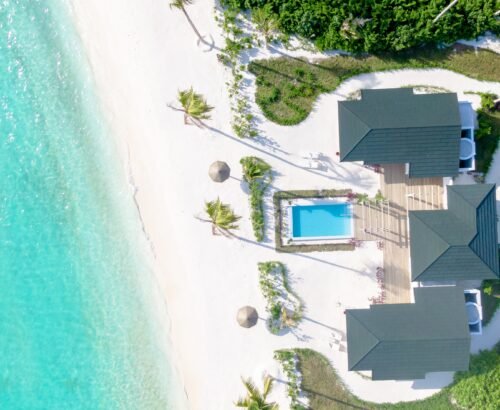 Aerial view of a Beach Residence at Joy Island Maldives featuring a private pool, wooden deck, multiple roof sections, and direct access to the white sand beach and turquoise lagoon