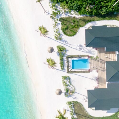 Aerial view of a Beach Residence at Joy Island Maldives featuring a private pool, wooden deck, multiple roof sections, and direct access to the white sand beach and turquoise lagoon