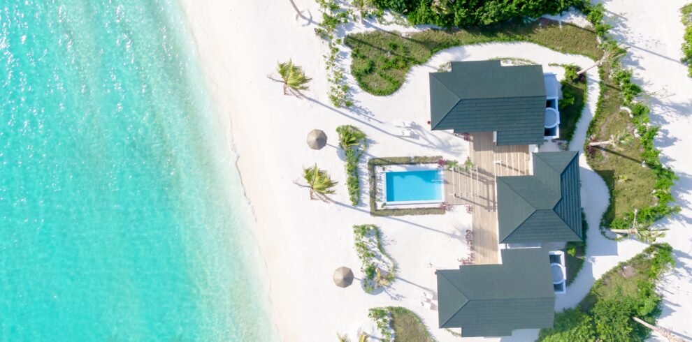 Aerial view of a Beach Residence at Joy Island Maldives featuring a private pool, wooden deck, multiple roof sections, and direct access to the white sand beach and turquoise lagoon