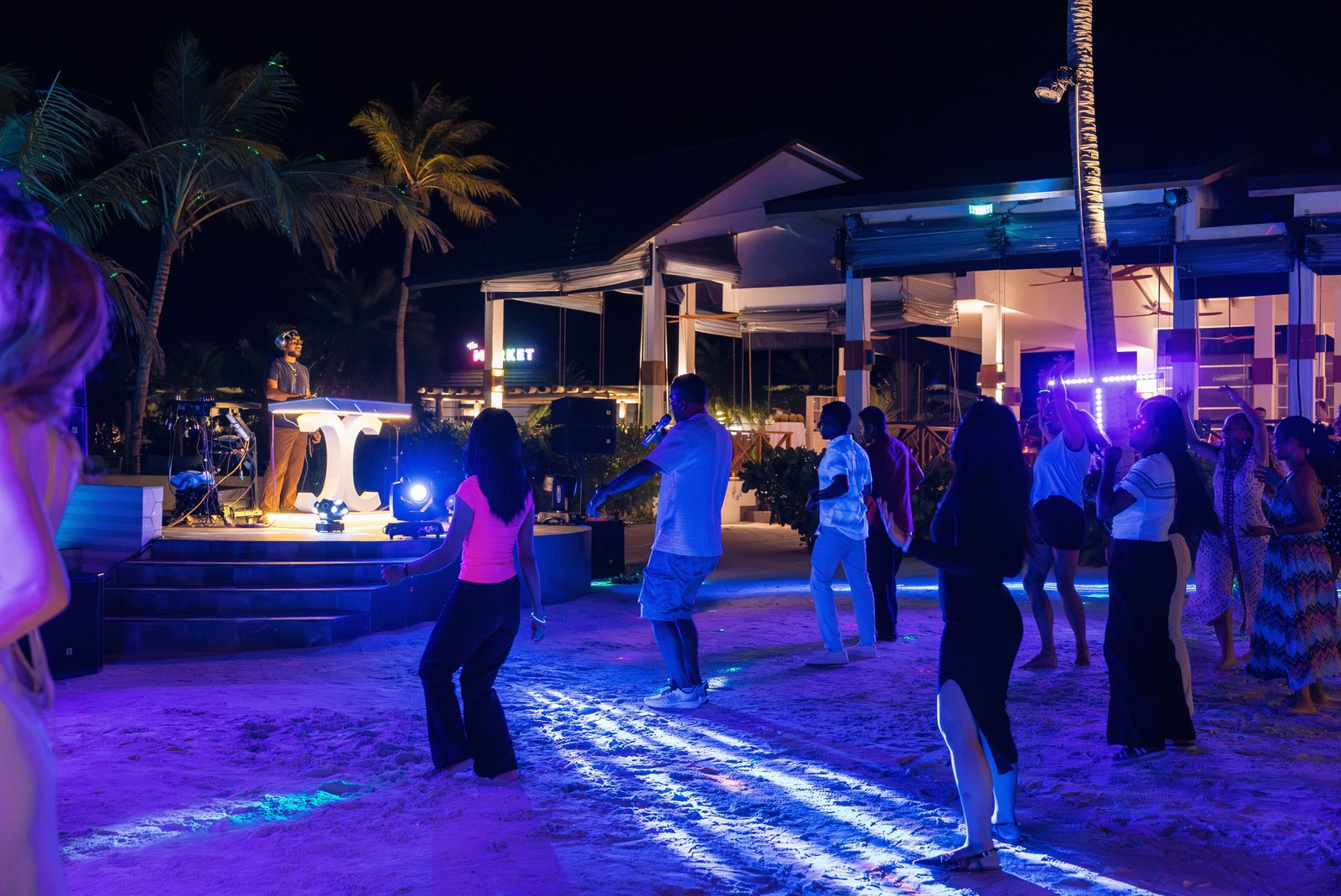 Guests dancing on the beach under colorful lights at a Glow Party event on Joy Island Maldives with DJ stage and palm trees at night