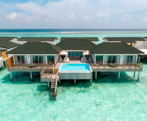 Aerial view of a Lagoon Residence at Joy Island Maldives featuring a private rectangular pool, wooden decks, and surrounding clear turquoise lagoon under a blue sky