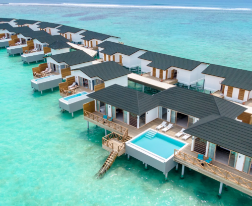 Aerial view of Lagoon Residences with private pools at Joy Island Maldives set over the clear turquoise lagoon with wooden decks and open ocean beyond