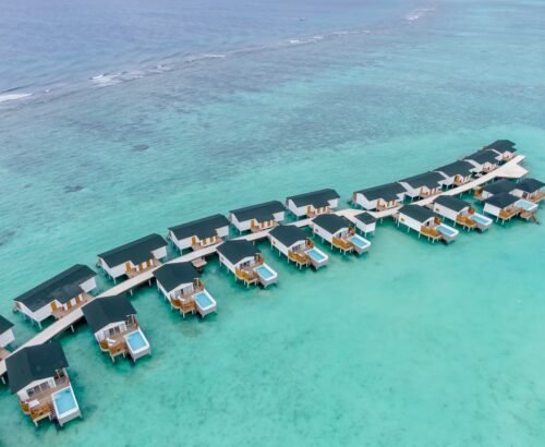 Aerial view of Lagoon Suites with private pools at Joy Island Maldives arranged along a jetty over the clear turquoise lagoon stretching toward the open ocean