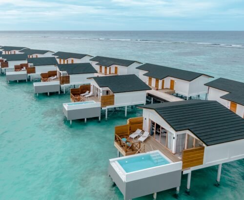 Aerial view of Lagoon Suites with private pools at Joy Island Maldives stretching over the clear turquoise lagoon toward the open ocean