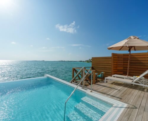 Private pool on the overwater deck of a Lagoon Suite at Joy Island Maldives with sun loungers, umbrella, and open views of the turquoise ocean under a clear blue sky