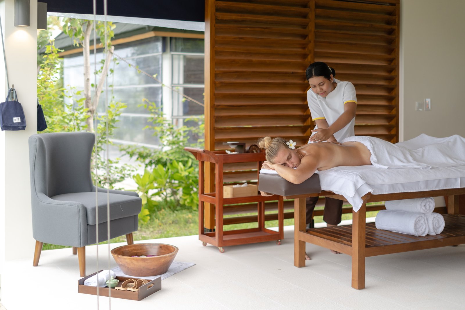 Woman receiving a relaxing massage at Oasis Spa on Joy Island Maldives in a bright treatment room with wooden screens and tropical garden views
