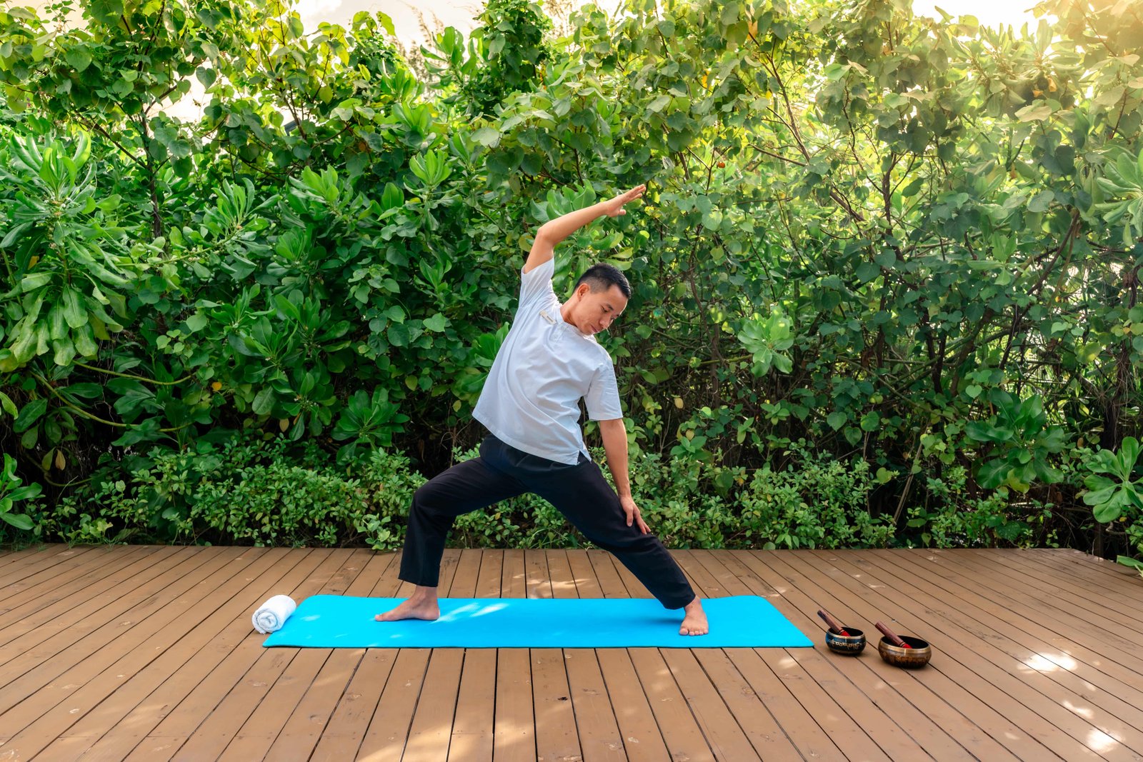Man practicing yoga on a wooden deck surrounded by lush green tropical plants at Joy Island Maldives during a wellness session