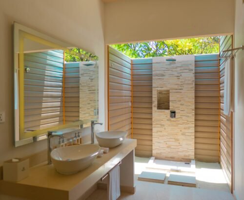 Beach Pool Villa bathroom at Brennia Kottefaru Maldives featuring dual white vessel sinks on a clean vanity and an open stone-tiled outdoor shower with natural light