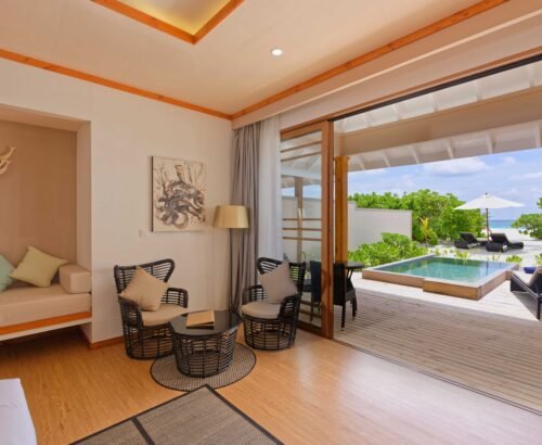 Beach Pool Villa interior at Brennia Kottefaru Maldives with a seating area and open sliding doors leading to a private pool, wooden deck, and beach views