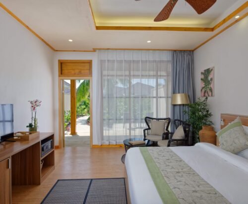 Bright Bougain Villa bedroom at Brennia Kottefaru Maldives with a large bed, wooden furniture, seating area by the window, and views of tropical greenery outside
