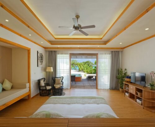 Spacious Deluxe Beach Pool Villa bedroom at Brennia Kottefaru Maldives with a large bed, seating area, and open sliding doors leading to a private pool and outdoor deck
