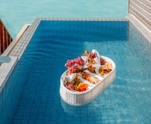 Floating breakfast tray filled with fresh fruits, flowers, and pastries in the private pool of a Deluxe Water Pool Villa at Brennia Kottefaru Maldives