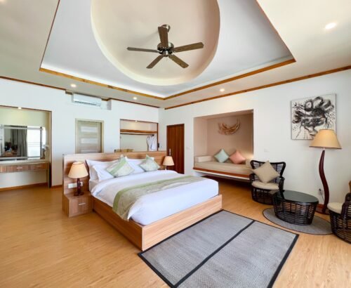 Spacious Deluxe Water Pool Villa bedroom at Brennia Kottefaru Maldives with a large wooden bed, seating area, open wardrobe, and warm natural lighting