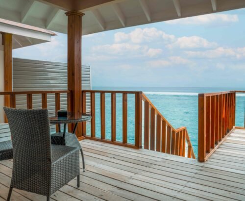 Private wooden deck of a Deluxe Water Villa at Brennia Kottefaru Maldives with outdoor seating and open views of the turquoise ocean under a blue sky