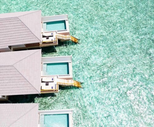 Aerial view of Ocean Pool Villas at Brennia Kottefaru Maldives with private rectangular pools extending over the clear turquoise lagoon and wooden stairs leading into the water