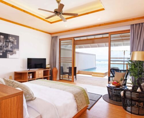 Ocean Pool Villa bedroom at Brennia Kottefaru Maldives with a large bed, seating area, and open sliding doors leading to a private infinity pool and turquoise ocean views