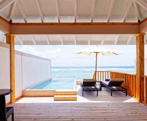 Ocean Pool Villa private deck at Brennia Kottefaru Maldives featuring an infinity-style pool, wooden sun loungers, white umbrella, and open views of the turquoise ocean