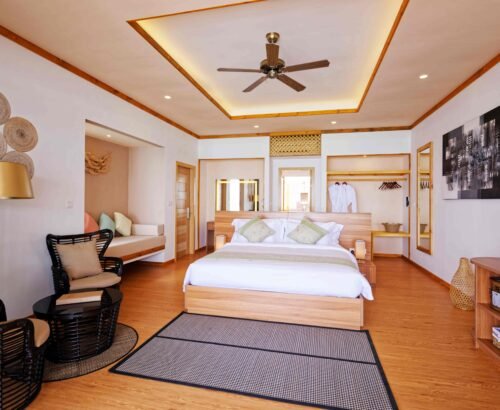 Spacious Ocean Pool Villa bedroom at Brennia Kottefaru Maldives with a large wooden bed, open wardrobe, seating area, and warm natural lighting