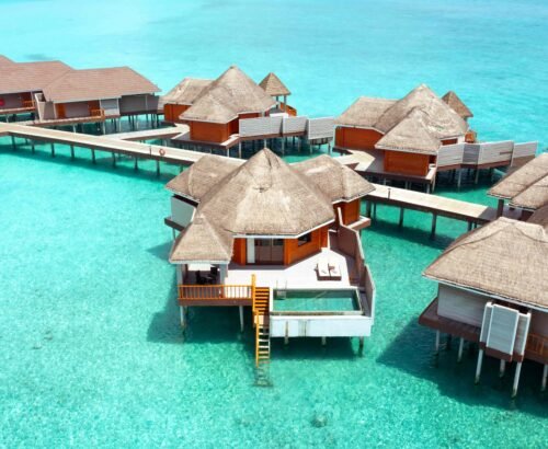 Aerial view of Over Water Suites with Pool at Brennia Kottefaru Maldives featuring thatched roofs, private pools, and wooden decks set above the clear turquoise lagoon