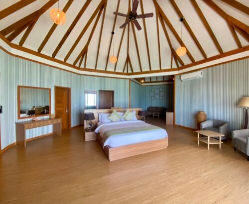 Spacious Over Water Suite with Pool bedroom at Brennia Kottefaru Maldives featuring a high vaulted wooden ceiling, large bed, seating area, and soft natural light