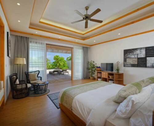 Spacious bedroom in a Two Bedroom Beach Pool Residence at Brennia Kottefaru Maldives with a large bed, seating area, and open sliding doors leading to a private outdoor deck with sun loungers