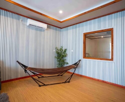 Indoor hammock area in a Two Bedroom Beach Pool Residence at Brennia Kottefaru Maldives featuring a brown hammock stand, striped walls, wooden flooring, and soft natural light