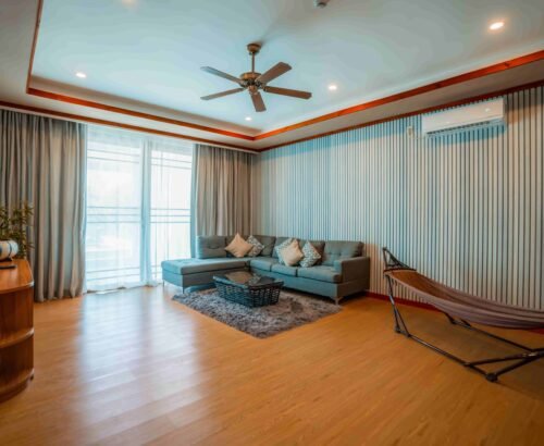 Spacious living area in a Two Bedroom Beach Pool Residence at Brennia Kottefaru Maldives featuring a grey sectional sofa, coffee table, indoor hammock, and large windows with soft natural light