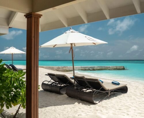 Beachfront sun loungers under white umbrellas outside a Two Bedroom Beach Villa at Brennia Kottefaru Maldives with soft white sand and turquoise lagoon views
