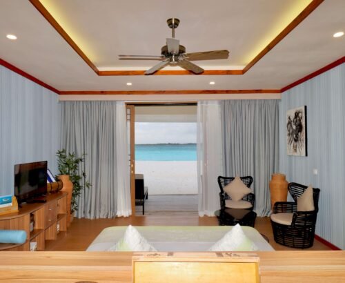 Bedroom in a Two Bedroom Beach Villa at Brennia Kottefaru Maldives with a large bed, seating area, and open sliding doors leading directly to the white sand beach and turquoise lagoon