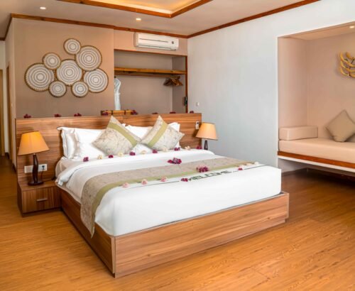 Spacious bedroom in a Two Bedroom Beach Villa at Brennia Kottefaru Maldives featuring a large wooden bed decorated with flower petals, open wardrobe, daybed, and warm soft lighting