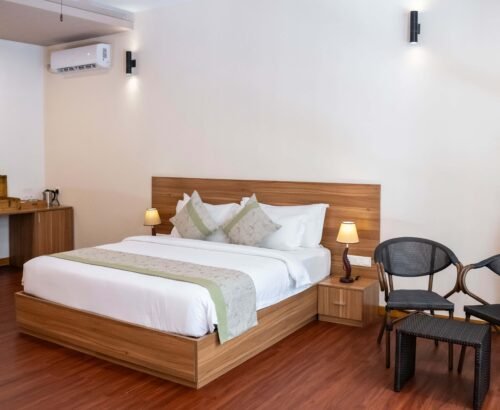 Bedroom in a Two Bedroom Bougain Villa at Brennia Kottefaru Maldives featuring a large wooden bed, bedside lamps, seating area with two chairs, and warm soft lighting