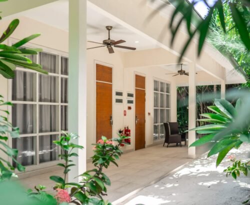 Entrance of a Two Bedroom Bougain Villa at Brennia Kottefaru Maldives featuring a covered porch, wooden doors, large windows, and surrounding tropical greenery