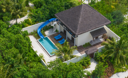 Aerial view of the Two Bedroom Garden Residence at dusitD2 Feydhoo Resort Maldives featuring a private swimming pool, blue water slide, wooden deck with sun loungers, thatched roof, and surrounding tropical greenery – ideal for a Maldives tour package family stay.
