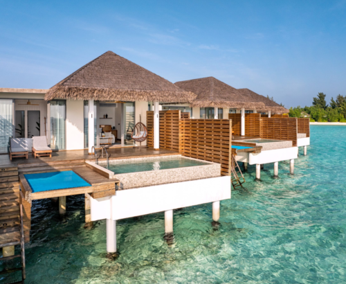 Overwater pool villas at dusitD2 Feydhoo Resort Maldives featuring thatched roofs, private swimming pools, wooden decks with sun loungers, hanging chairs, and direct access to crystal-clear turquoise lagoon waters under a bright blue sky – perfect for a Maldives tour package.