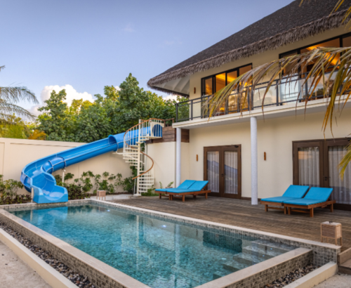 Two Bedroom Garden Residence at dusitD2 Feydhoo Resort Maldives featuring a private swimming pool, blue water slide, wooden deck with sun loungers, spiral staircase, and two-story villa with thatched roof under a soft evening sky – perfect for a Maldives tour package family stay.