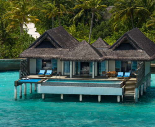 Two Bedroom Party Suite overwater villa at dusitD2 Feydhoo Resort Maldives featuring thatched roofs, large private swimming pool, wooden decks with sun loungers, outdoor dining area, and stilts above the turquoise lagoon surrounded by palm trees – perfect for a Maldives tour package.